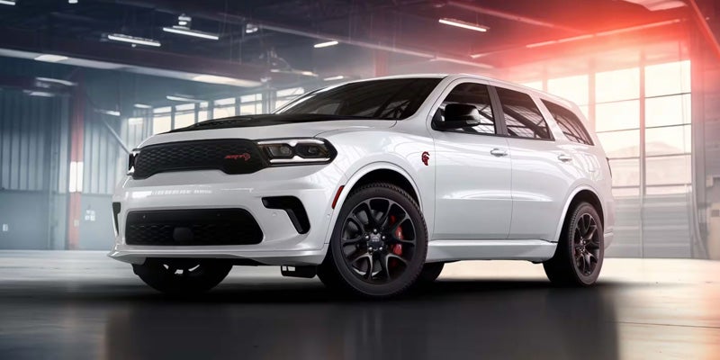 A white Dodge Durango SRT Hellcat SUV with a black hood stripe, black rims, and red brake calipers in a garage.