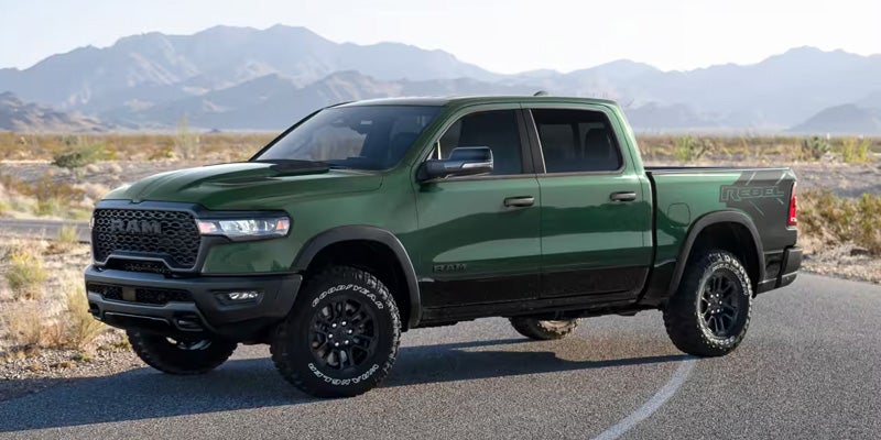 A green Ram Rebel pickup truck with black accents and aggressive off-road tires parked on an asphalt road.