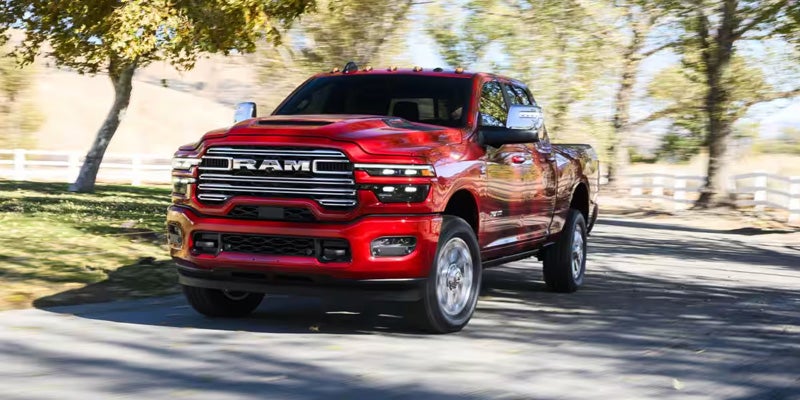 A red Ram 2500 Heavy Duty Laramie pick-up truck drives towards the viewer on a tree-lined asphalt road.